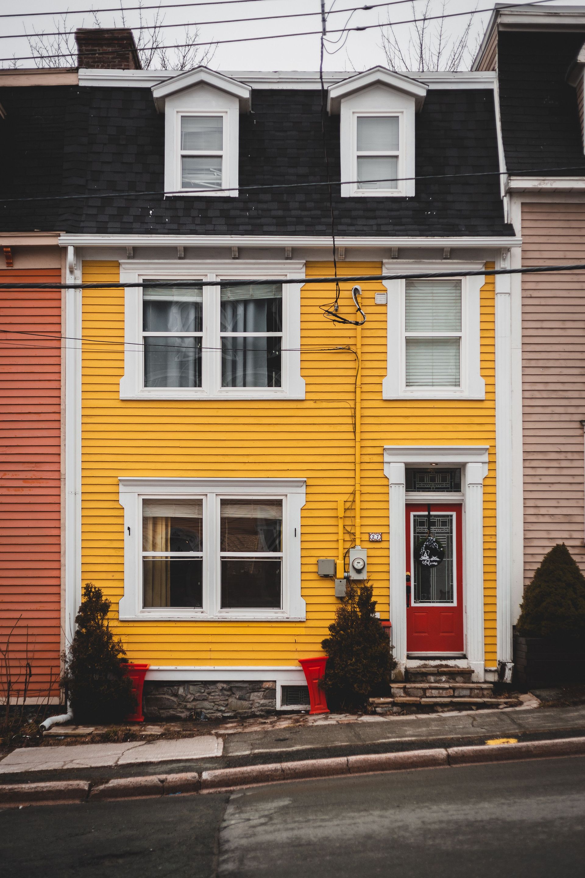 Facade of yellow old fashioned residential building located near sidewalk with green plants and asphalt road on street of town